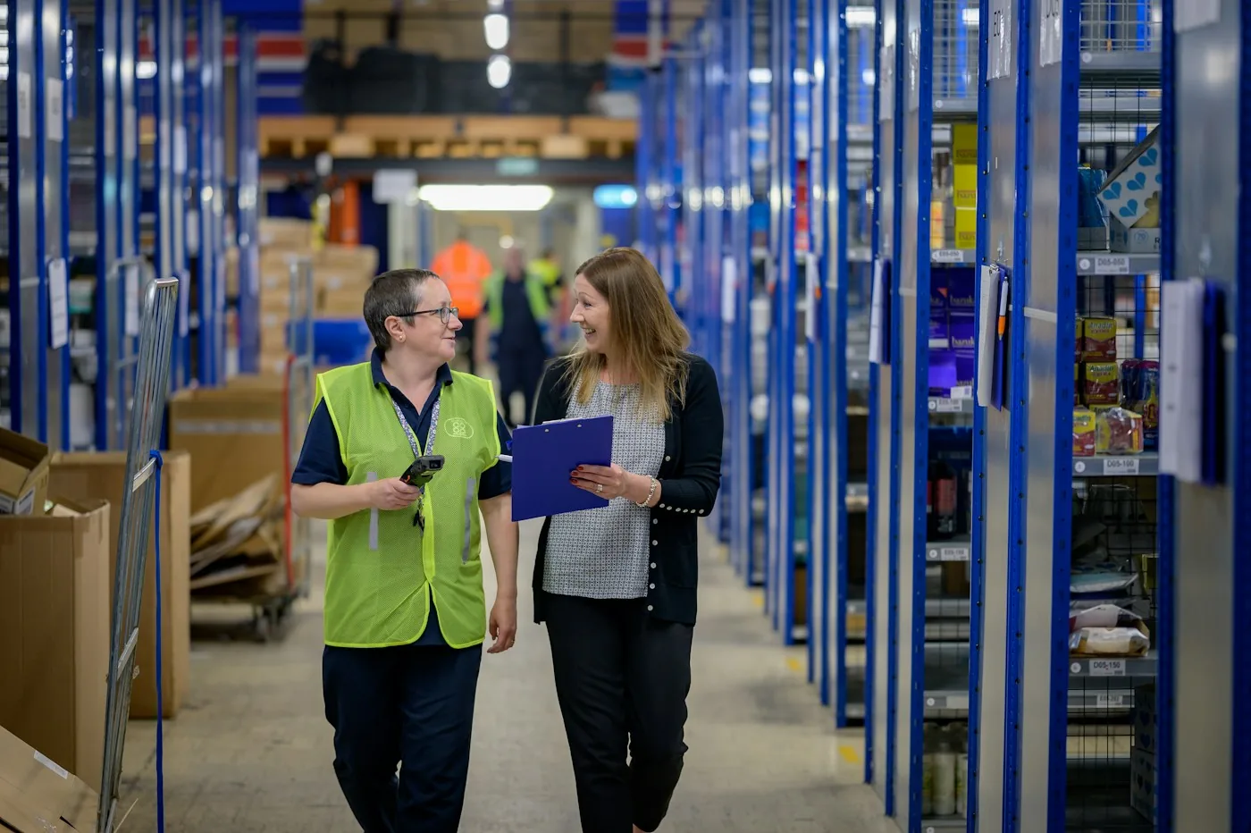 Two warehouse professionals reviewing records beside inventory.